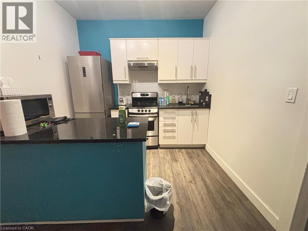 Kitchen with appliances with stainless steel finishes, white cabinets, under cabinet range hood, and tasteful backsplash - 25 Main Street Unit# 302, Cambridge, ON - Indoor Photo Showing Kitchen