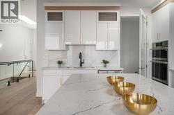 Kitchen with light stone counters, white cabinetry, a skylight, decorative backsplash, and double oven -