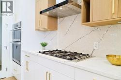 Kitchen with exhaust hood, light stone counters, stainless steel appliances, and backsplash -