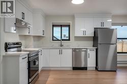 Kitchen with stainless steel appliances, white cabinetry, under cabinet range hood, and light wood-style flooring -