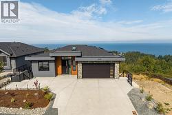 View of front of home with concrete driveway, a garage, stone siding, a water view, and a shingled roof -
