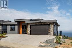 Modern home featuring stone siding, driveway, and an attached garage -