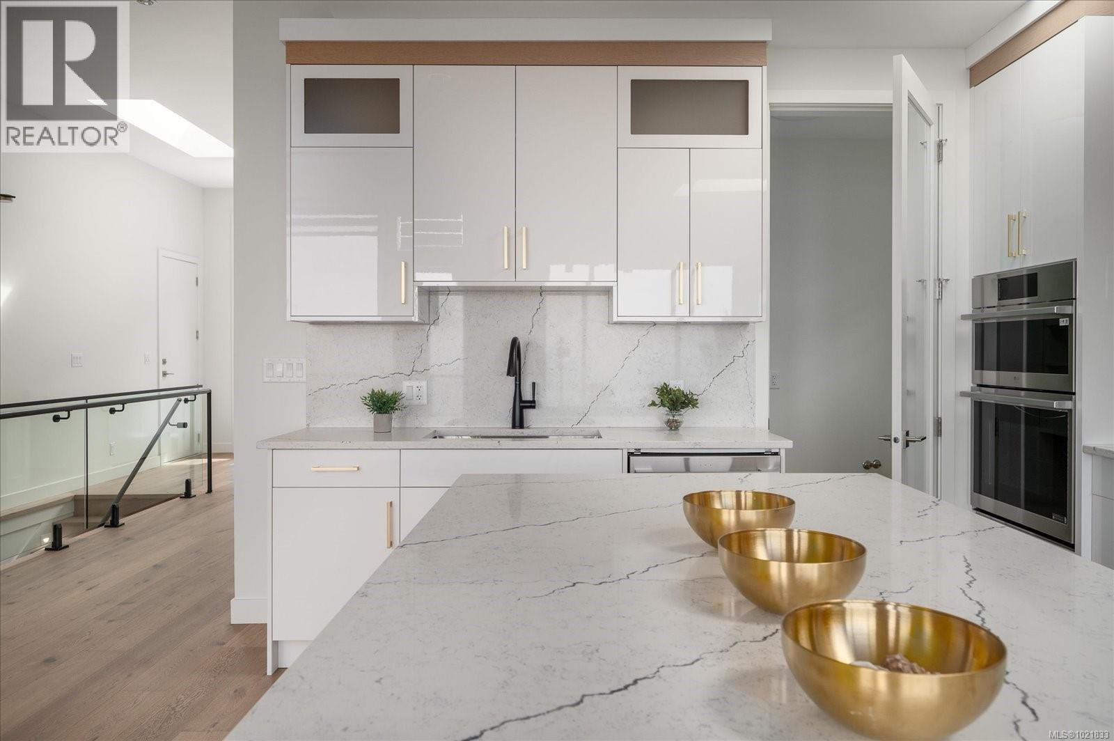 Kitchen with light stone counters, white cabinetry, a skylight, decorative backsplash, and double oven - 4680 Ambience Dr, Nanaimo, BC - Indoor Photo Showing Kitchen