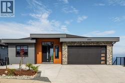 Contemporary home featuring stone siding, a garage, and concrete driveway -