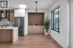 Kitchen featuring high quality fridge, wall chimney exhaust hood, decorative light fixtures, light stone counters, and light wood-style flooring -