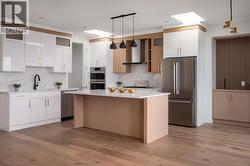 Kitchen with decorative light fixtures, stainless steel appliances, light stone countertops, wall chimney exhaust hood, and white cabinetry -