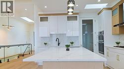 Kitchen featuring a skylight, hanging light fixtures, light stone counters, exhaust hood, and recessed lighting -