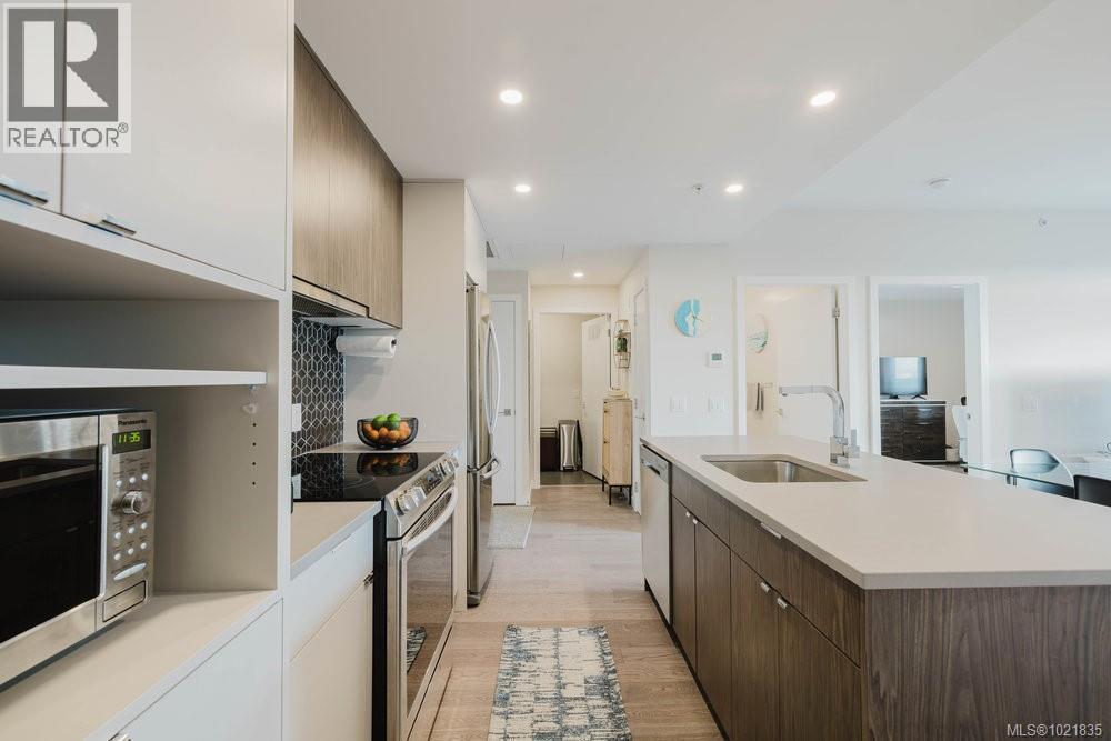 Kitchen with appliances with stainless steel finishes, modern cabinets, light wood-type flooring, recessed lighting, and a center island with sink - 210 881 Short St, Saanich, BC - Indoor Photo Showing Kitchen