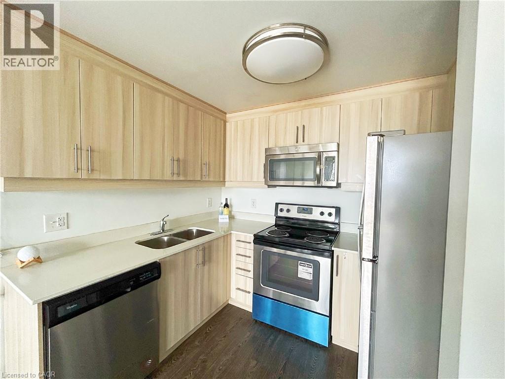 Kitchen featuring light brown cabinetry, stainless steel appliances, dark wood finished floors, and light stone counters - 158 King Street N Unit# 1504, Waterloo, ON - Indoor Photo Showing Kitchen With Double Sink