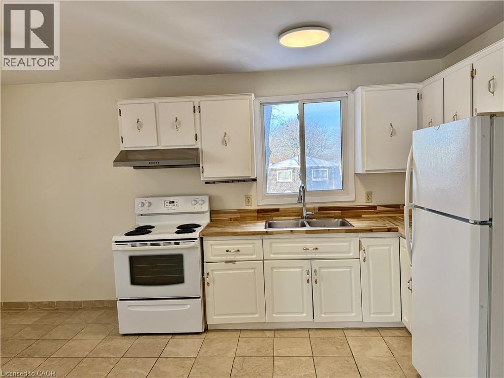 Kitchen featuring white appliances, white cabinetry, under cabinet range hood, and light tile patterned flooring - 79 Lillian Drive Unit# A, Waterloo, ON - Indoor Photo Showing Kitchen With Double Sink