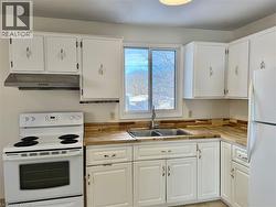 Kitchen with white appliances, white cabinetry, under cabinet range hood, and light tile patterned floors -
