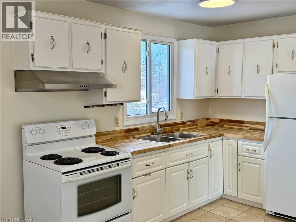 Kitchen with white appliances, white cabinetry, under cabinet range hood, and light tile patterned floors - 79 Lillian Drive Unit# A, Waterloo, ON - Indoor Photo Showing Kitchen With Double Sink