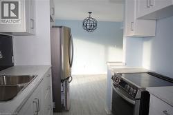 Kitchen with white cabinetry, stainless steel appliances, a chandelier, decorative light fixtures, and light stone countertops -