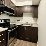 Kitchen with appliances with stainless steel finishes, dark brown cabinets, light countertops, and light wood finished floors -