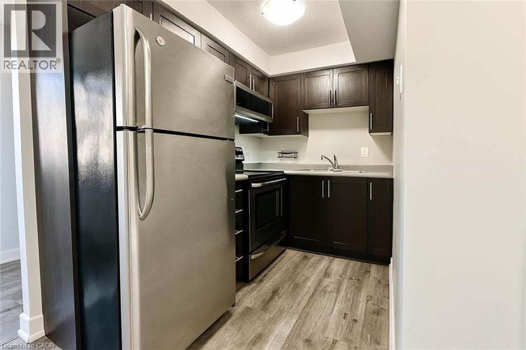 Kitchen with appliances with stainless steel finishes, light countertops, light wood-type flooring, dark brown cabinetry, and a textured ceiling - 185 Windale Crescent Unit# 5A, Kitchener, ON - Indoor Photo Showing Kitchen With Double Sink