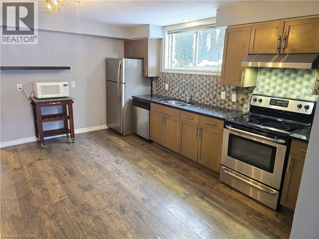 Kitchen with appliances with stainless steel finishes, brown cabinetry, under cabinet range hood, and dark wood-style flooring - 50 Scenic Drive Unit# Lower, Kitchener, ON - Indoor Photo Showing Kitchen With Double Sink