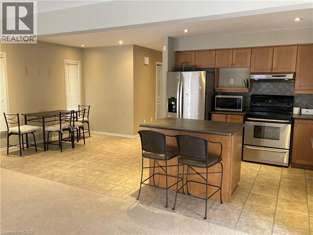 Kitchen with stainless steel appliances, recessed lighting, brown cabinetry, light tile patterned floors, and dark countertops - 421 White Birch Avenue, Waterloo, ON - Indoor Photo Showing Kitchen