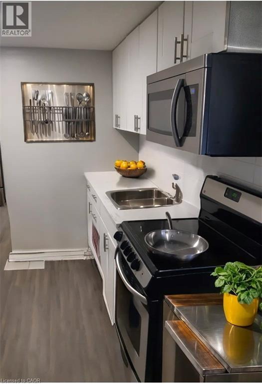 Kitchen featuring stainless steel appliances, white cabinets, light countertops, and dark wood-style flooring - 70 Victoria Avenue S Unit# 5, Hamilton, ON - Indoor Photo Showing Kitchen