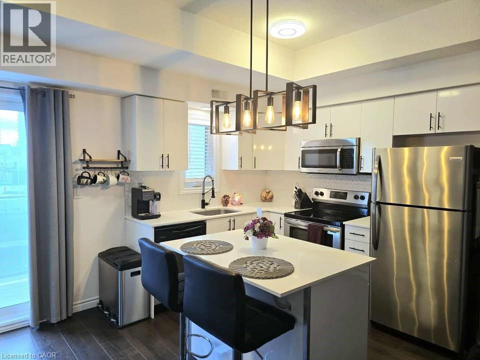 Kitchen with appliances with stainless steel finishes, decorative light fixtures, a kitchen island, a kitchen bar, and white cabinetry - 1430 Highland Road W Unit# 7C, Kitchener, ON - Indoor Photo Showing Kitchen With Stainless Steel Kitchen