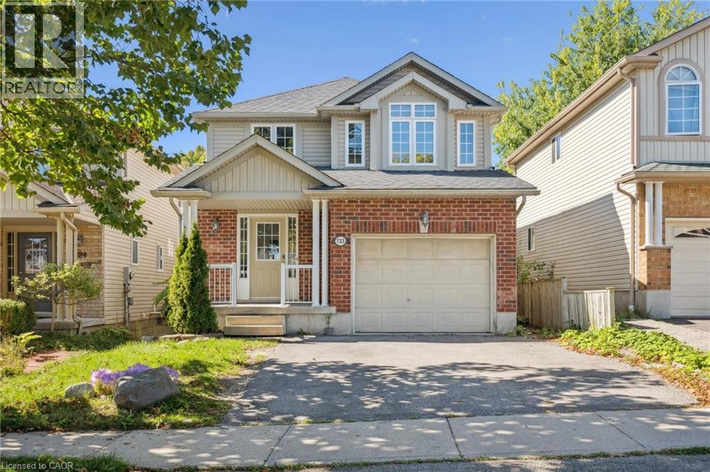 View of front of property featuring covered porch, driveway, brick siding, a garage, and a shingled roof - 723 Black Cherry Street, Waterloo, ON - Outdoor With Facade