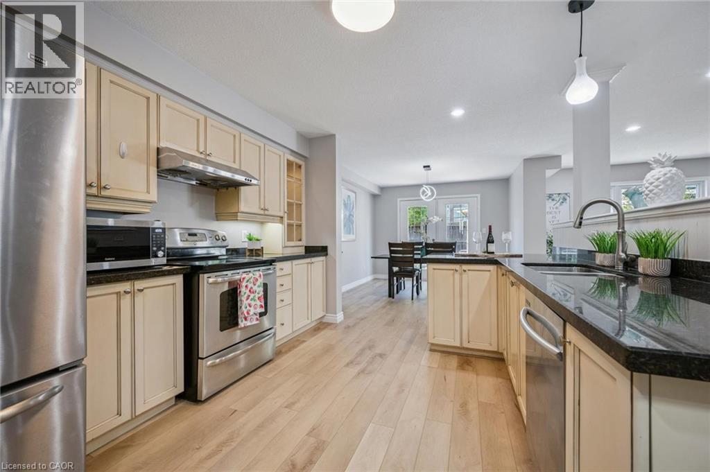 Kitchen with stainless steel appliances, decorative light fixtures, light wood-style flooring, dark stone counters, and recessed lighting - 723 Black Cherry Street, Waterloo, ON - Indoor Photo Showing Kitchen With Stainless Steel Kitchen With Upgraded Kitchen