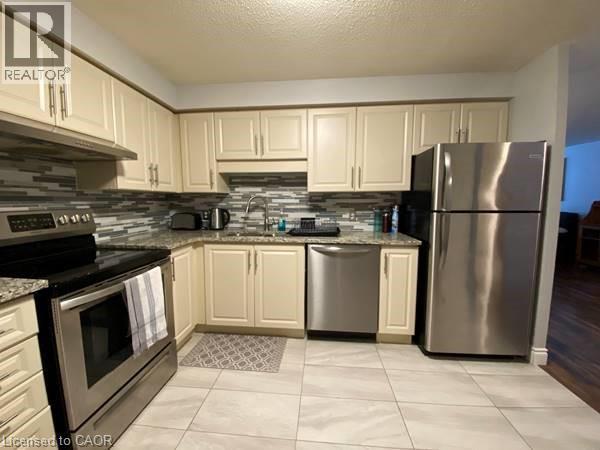 Kitchen with appliances with stainless steel finishes, decorative backsplash, a textured ceiling, light tile patterned floors, and light stone counters - 35 Green Valley Drive Unit# 414, Kitchener, ON - Indoor Photo Showing Kitchen