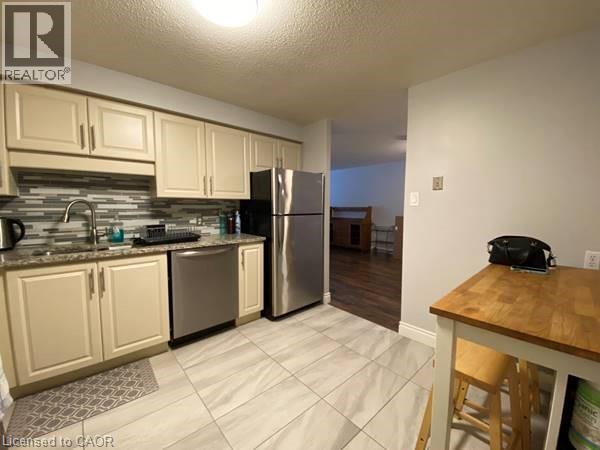 Kitchen featuring cream cabinetry, stainless steel appliances, a textured ceiling, decorative backsplash, and dark stone counters - 35 Green Valley Drive Unit# 414, Kitchener, ON - Indoor Photo Showing Kitchen