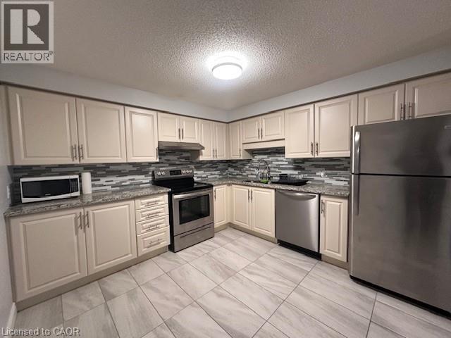 Kitchen with stainless steel appliances, a textured ceiling, light stone countertops, backsplash, and under cabinet range hood - 35 Green Valley Drive Unit# 414, Kitchener, ON - Indoor Photo Showing Kitchen