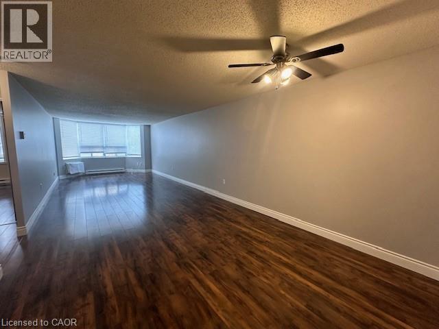 Empty room featuring a textured ceiling, dark wood-style flooring, and ceiling fan - 35 Green Valley Drive Unit# 414, Kitchener, ON - Indoor Photo Showing Other Room