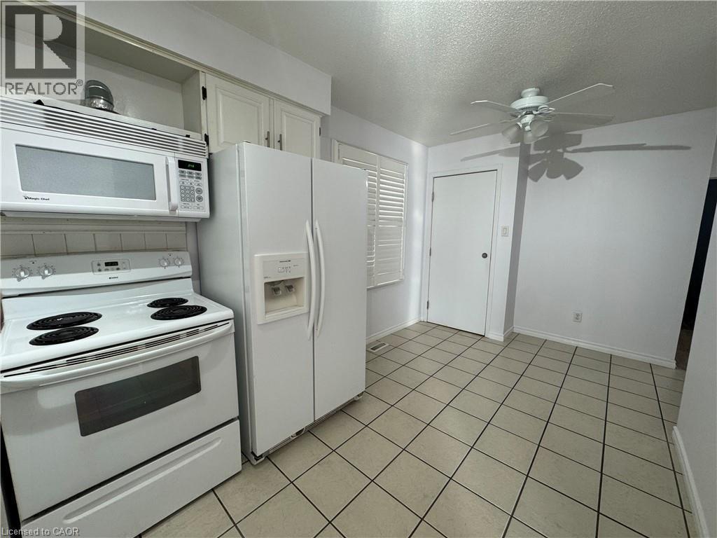 Kitchen with white appliances, a textured ceiling, a ceiling fan, white cabinetry, and light tile patterned floors - 86 Hillsborough Crescent Unit# Main, Kitchener, ON - Indoor Photo Showing Kitchen