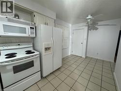 Kitchen with white appliances, a textured ceiling, a ceiling fan, white cabinetry, and light tile patterned floors -