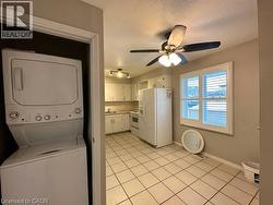 Laundry room featuring stacked washing machine and dryer, light tile patterned floors, and a ceiling fan -