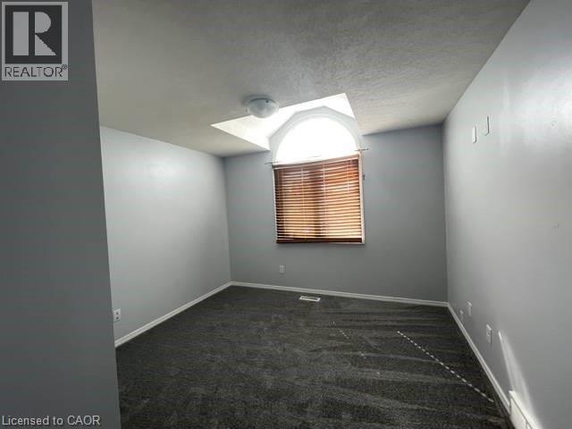 Empty room featuring a textured ceiling, dark carpet, and a baseboard radiator - 214 Benesfort Crescent, Kitchener, ON - Indoor Photo Showing Other Room