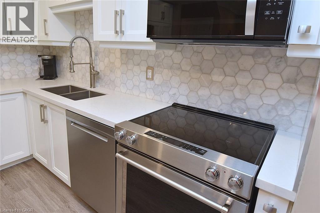 Kitchen featuring appliances with stainless steel finishes, white cabinets, tasteful backsplash, light stone counters, and light wood-type flooring - 1245 Stephenson Drive Unit# 20, Burlington, ON