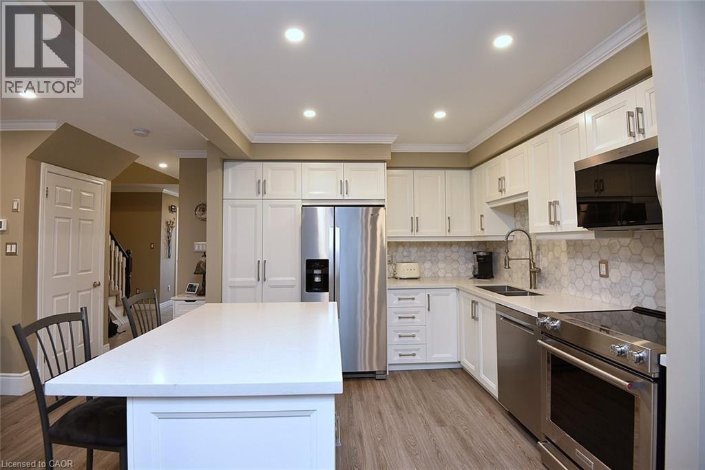 Kitchen with appliances with stainless steel finishes, crown molding, white cabinets, light stone countertops, and a center island - 1245 Stephenson Drive Unit# 20, Burlington, ON