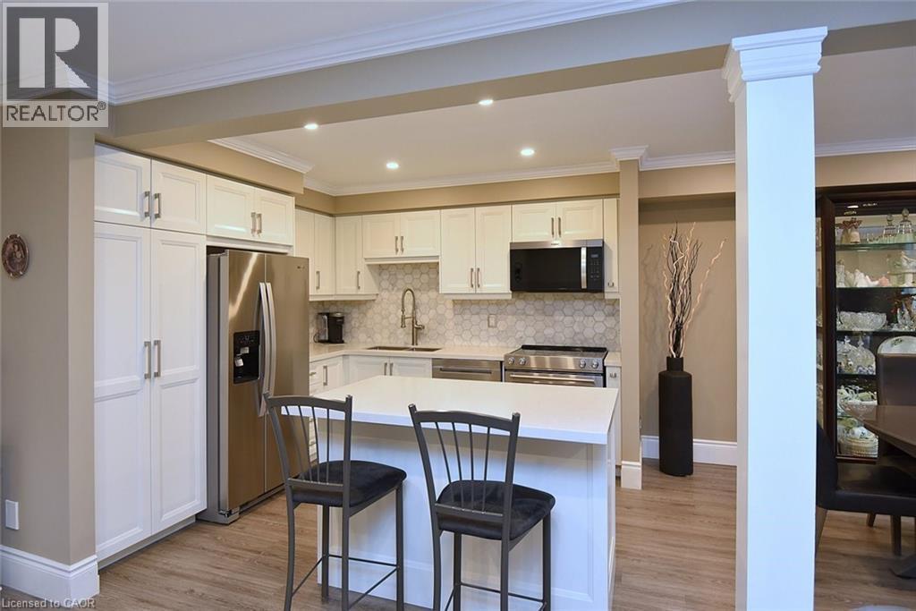 Kitchen with stainless steel appliances, white cabinets, a kitchen island, a kitchen bar, and backsplash - 1245 Stephenson Drive Unit# 20, Burlington, ON