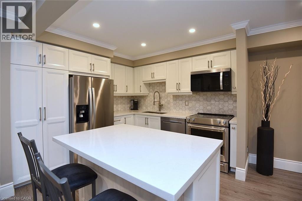 Kitchen featuring white cabinets, stainless steel appliances, ornamental molding, tasteful backsplash, and a kitchen bar - 1245 Stephenson Drive Unit# 20, Burlington, ON