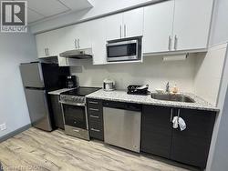Kitchen featuring white cabinetry, stainless steel appliances, light wood-type flooring, and under cabinet range hood -