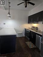 Kitchen with dark cabinetry, hanging light fixtures, stove, dishwasher, and exhaust hood -