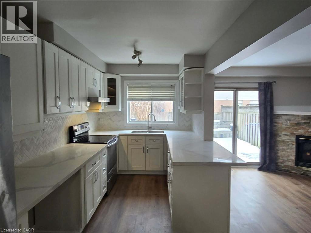 Kitchen with stainless steel range with electric stovetop, a peninsula, white cabinets, and dark wood-style flooring - 185 Sulmona Drive, Hamilton, ON - Indoor Photo Showing Kitchen With Fireplace