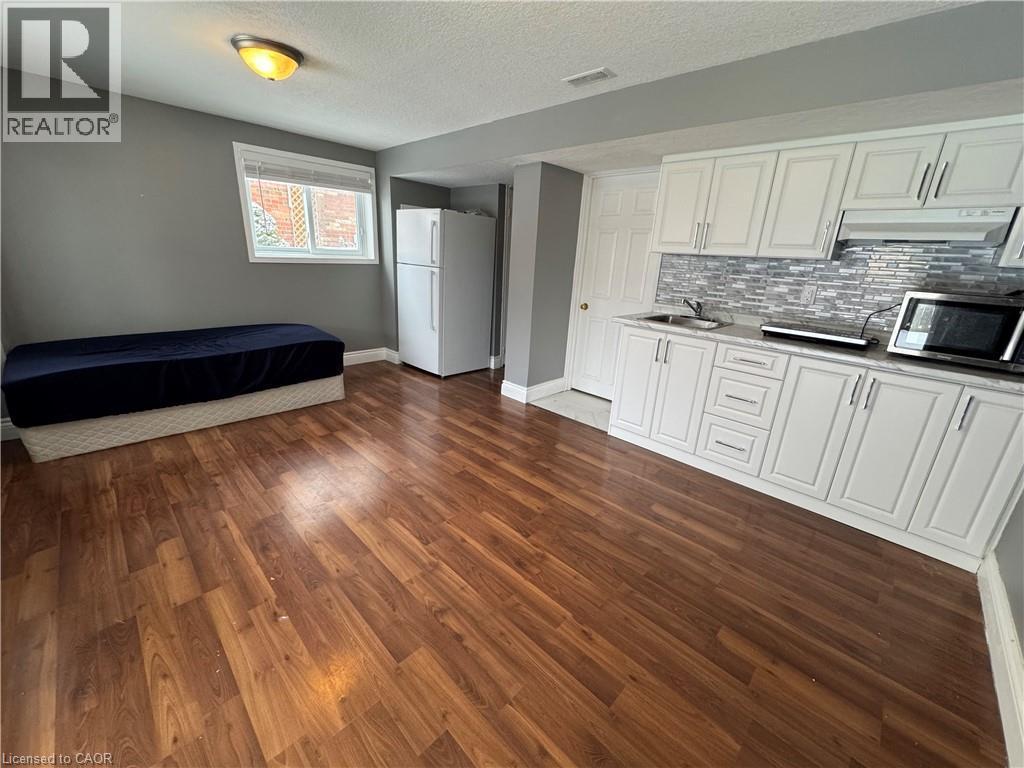 Kitchen featuring freestanding refrigerator, white cabinets, dark wood-type flooring, a textured ceiling, and stainless steel microwave - 211 Snowdrop Crescent Unit# Lower, Kitchener, ON - Indoor