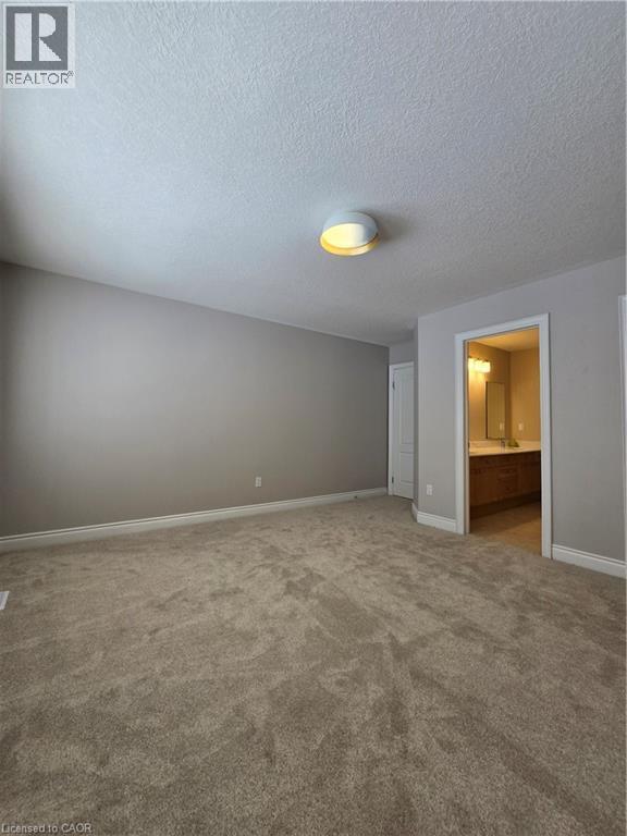 Unfurnished bedroom with carpet flooring, connected bathroom, and a textured ceiling - 93 Tremaine Drive, Kitchener, ON - Indoor Photo Showing Other Room