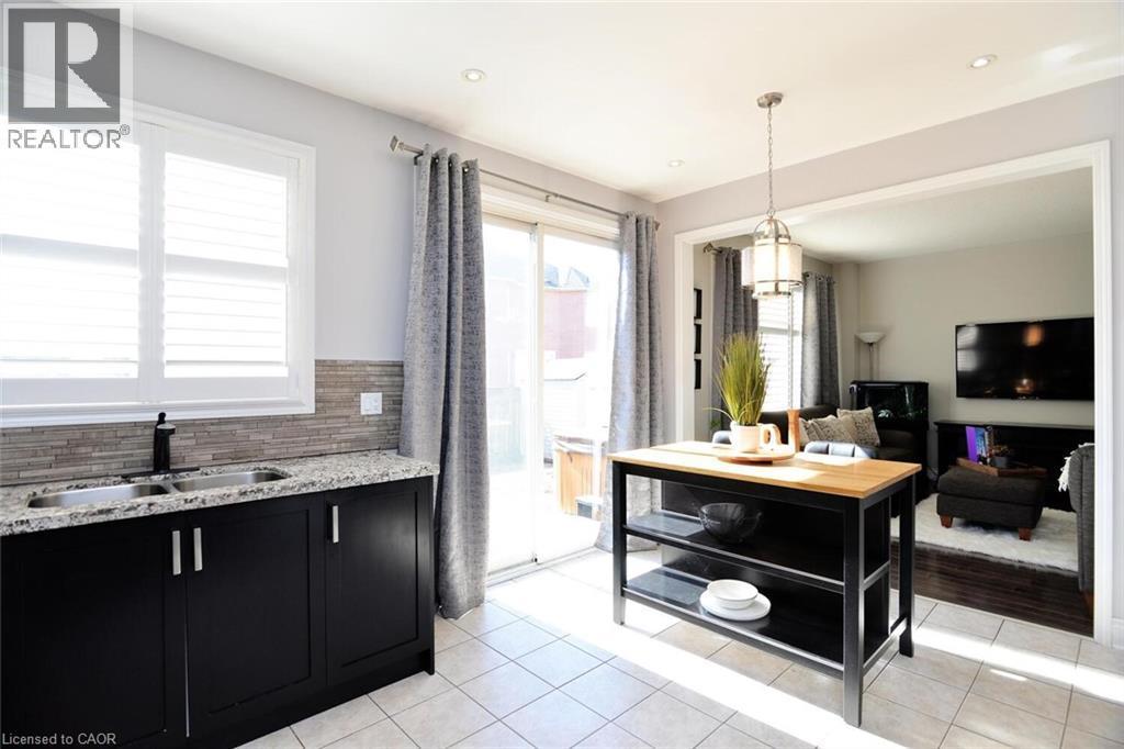 Kitchen featuring dark cabinets, hanging light fixtures, light stone counters, light tile patterned floors, and backsplash - 49 Eberhardt Drive, Wasaga Beach, ON - Indoor Photo Showing Kitchen With Double Sink
