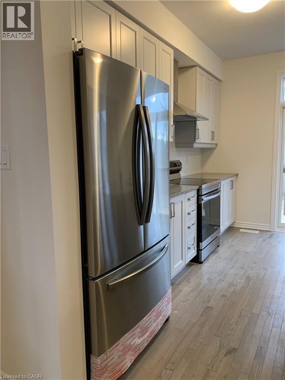 Kitchen featuring stainless steel appliances, light wood-style flooring, wall chimney range hood, and white cabinetry - 49 Eberhardt Drive, Wasaga Beach, ON - Indoor Photo Showing Kitchen