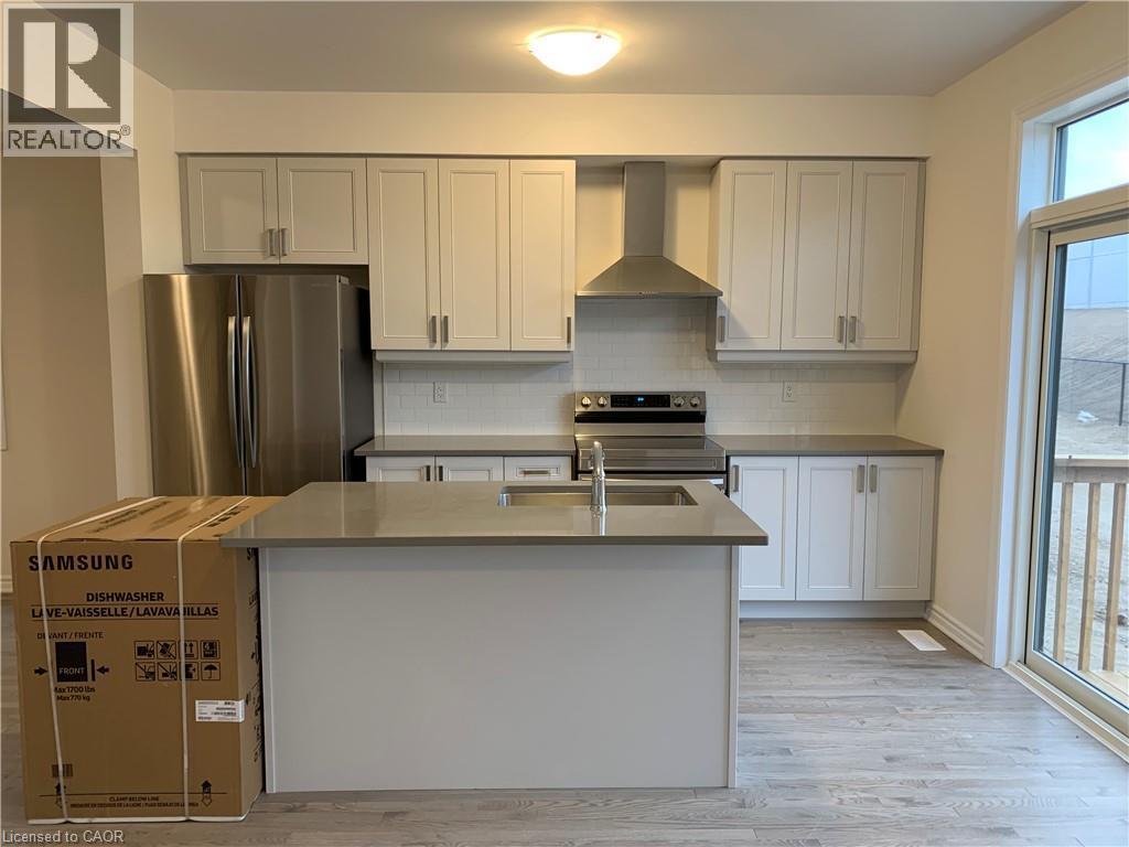 Kitchen featuring appliances with stainless steel finishes, wall chimney range hood, light wood-style floors, a kitchen island with sink, and decorative backsplash - 49 Eberhardt Drive, Wasaga Beach, ON - Indoor Photo Showing Kitchen With Double Sink