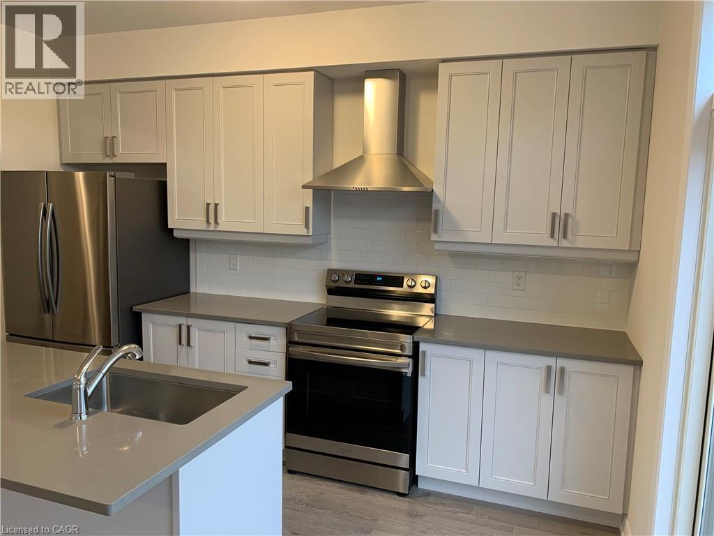 Kitchen featuring stainless steel appliances, wall chimney range hood, decorative backsplash, light wood-style floors, and dark stone countertops - 49 Eberhardt Drive, Wasaga Beach, ON - Indoor Photo Showing Kitchen
