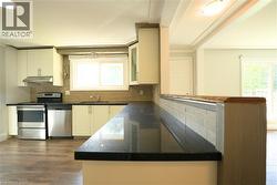 Kitchen featuring stainless steel appliances, white cabinetry, decorative backsplash, dark wood-type flooring, and under cabinet range hood -
