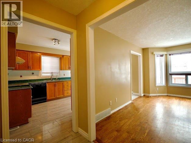 Kitchen featuring light wood finished floors, dishwasher, brown cabinets, decorative backsplash, and a textured ceiling - 109 Beechmanor Crescent, Kitchener, ON - Indoor