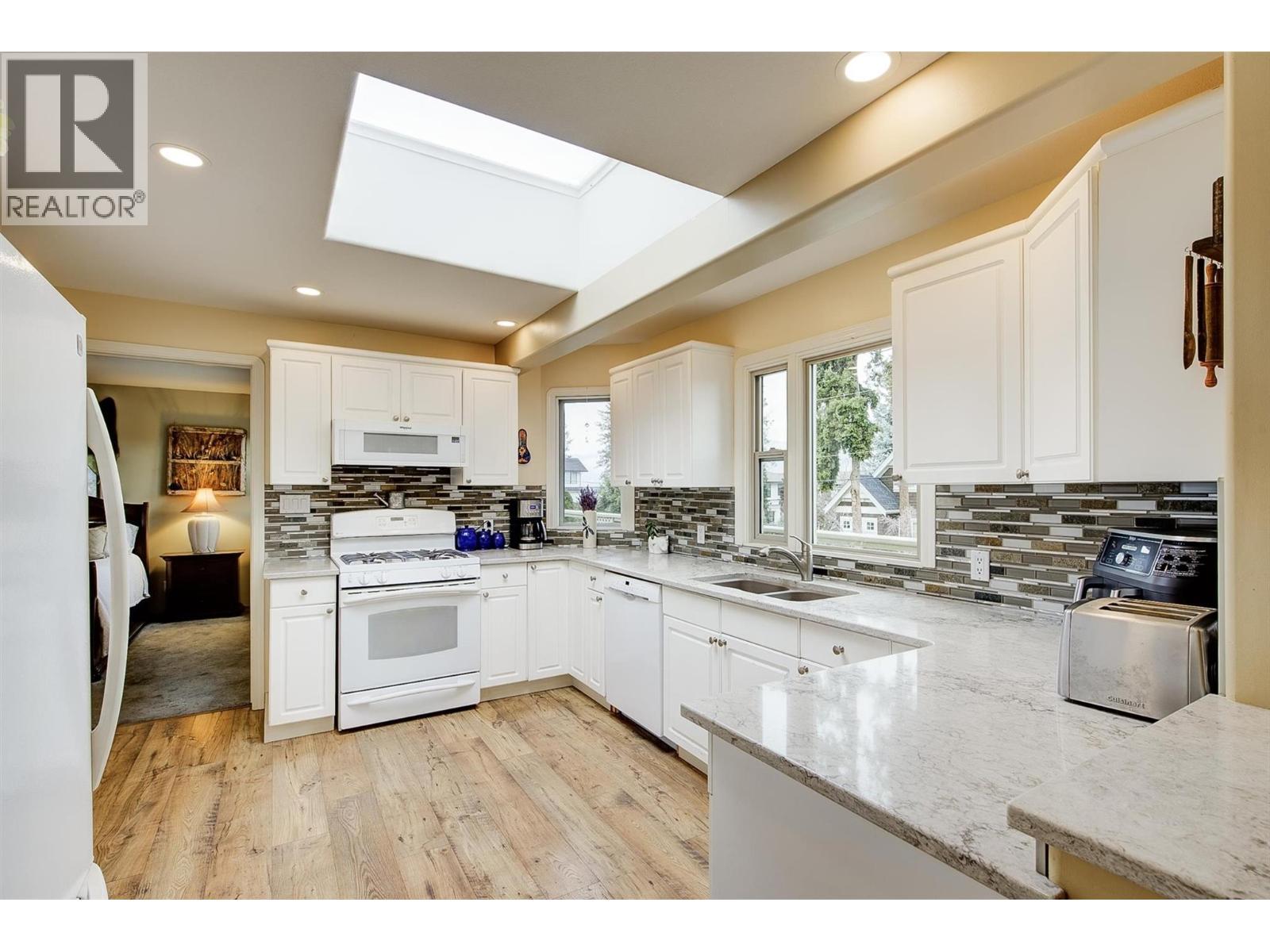 Functional and bright U-shaped kitchen with modern appliances and partial lake view from kitchen window - 391 Braeloch Road, Kelowna, BC - Indoor Photo Showing Kitchen With Double Sink