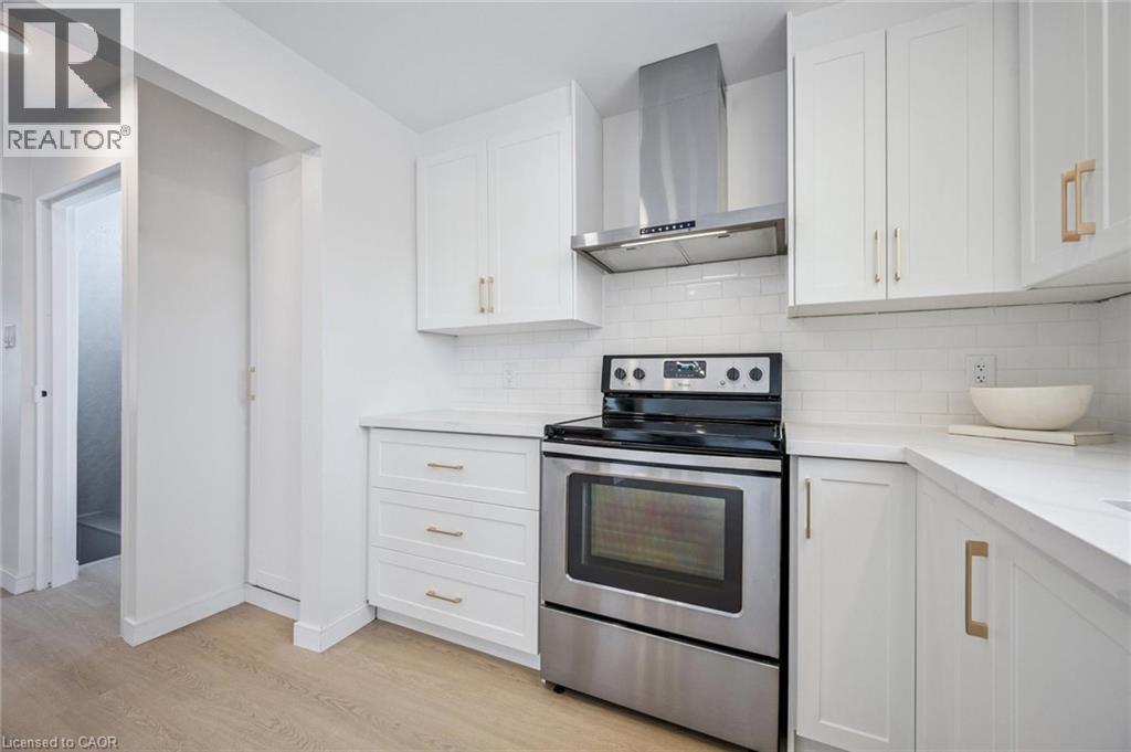 Kitchen with electric range, wall chimney range hood, white cabinets, tasteful backsplash, and light wood-style floors - 21 Forest Glen Court, Kitchener, ON - Indoor Photo Showing Kitchen